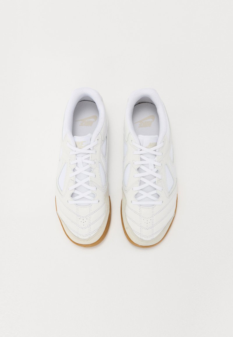 Zapatillas deportivas blancas con parte superior de cuero texturizado, detalles de malla y perforaciones. Suela de goma color crema con punta redondeada.