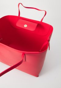 Saco tote de couro vermelho com textura suave, duas alças, fecho de botão e um interior espaçoso. Sem compartimentos ou padrões visíveis.