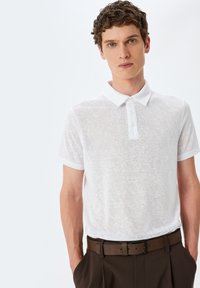 Hvid kortærmet polo skjorte med struktureret look, der har en klassisk krave og tre-knaps stolpe. Bæres med brune bukser og bælte.