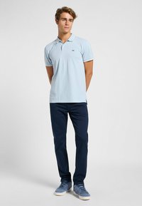 Ljusblå pikétröja med ribbad krage, kort ärm och sidospår, i kombination med marinblå byxor och blå sneakers.