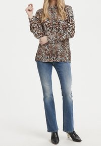 Blusa a stampa leopardata con maniche lunghe e chiusura a bottoni, abbinata a jeans blu e stivali neri con tacco. Tessuto morbido, vestibilità comoda.