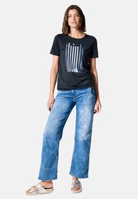 T-shirt noir à manches courtes avec un graphisme "think" en bleu clair, associé à un jean en denim bleu délavé et ample, et des sandales argentées.
