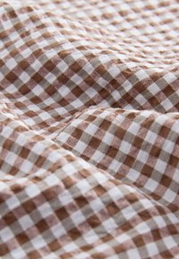 Rudos ir baltos spalvos languotas audinys, minkštos tekstūros, su smulkia gingham rašto danga ir raukšlėtu paviršiumi.