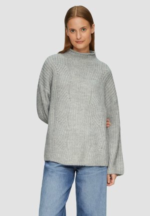 Pull en maille gris à col montant, silhouette ample et motif texturé. Associé à un jean large bleu clair.