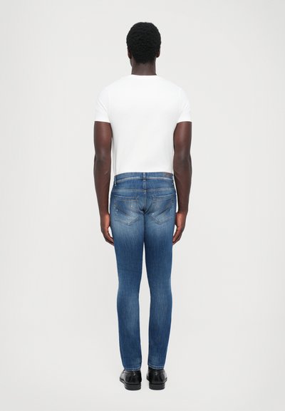 Jeans skinny blu in denim, caratterizzati da un lavaggio sbiadito, dettagli sottili sulle tasche e bordi consumati, abbinati a una semplice t-shirt bianca.