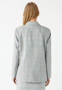 Blazer azzurro chiaro con motivo a quadri, con uno spacco posteriore, spalle strutturate e vestibilità su misura. Il tessuto ha una texture liscia.
