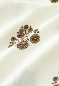 Bawełniana tkanina o białym tle, ozdobiona misternymi brązowymi wzorami kwiatowymi, charakteryzująca się gładką fakturą i lekkim układem.