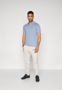Lyseblå polo t-shirt med et lille logo, parret med beige joggers med et mørkt logo og sorte løbesko. Renset, tætsiddende silhuet.