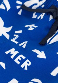 Blaue Schwimmshorts aus Stoff mit großen weißen Texten und Pfeilgrafiken, mit einem schwarzen Kordelzug an der Taille. Weicher Stoff und lässiges Design.