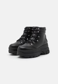 Botas de cuero negro hasta el tobillo con una suela plataforma gruesa, que presentan herrajes metálicos, cordones multihoyos y acolchado en el tobillo para mayor comodidad.