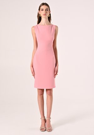 Abito aderente rosa con scollatura a barca e orlo a ginocchio. Tessuto liscio con dettagli delle cuciture laterali. Indossato con scarpe beige con cinturini.