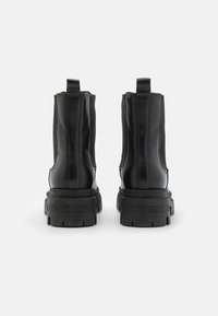 Bottines noires en cuir lisse avec des panneaux élastiques sur les côtés, une semelle épaisse solide et des languettes pour un enfilage facile.