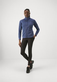 Fleece jacket in dark blue with zip closure and long sleeves, paired with black leggings and black athletic shoes featuring green accents.