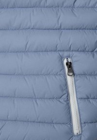 Doudoune en tissu bleu clair, présentant des lignes horizontales matelassées, une poche zippée avec des accessoires noirs à l'avant.