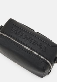 Černá taška z texturované kůže s embosovaným logem "VALENTINO". Disponuje kovovým zipem a rohovým tvarem, ideální pro každodenní používání.