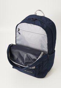 Granatowy plecak z zapinaną na zamek przednią kieszenią oraz przestronną komorą główną. Wykonany z trwałego materiału, z szarym wykończeniem wnętrza.