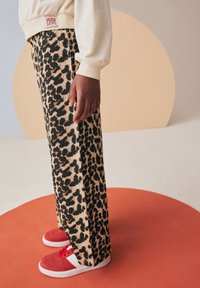 Pantaloni in maglia con stampa leopardata e tessuto testurizzato. Indossati con sneakers rosse con accenti bianchi su uno sfondo circolare arancione.
