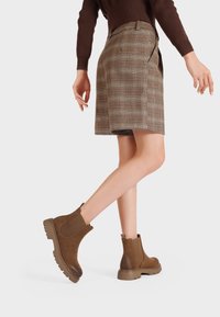 Stivaletti in suede marrone con pannelli elastici laterali, suole in gomma spesse e leggero lucido, indossati con una gonna a quadri.