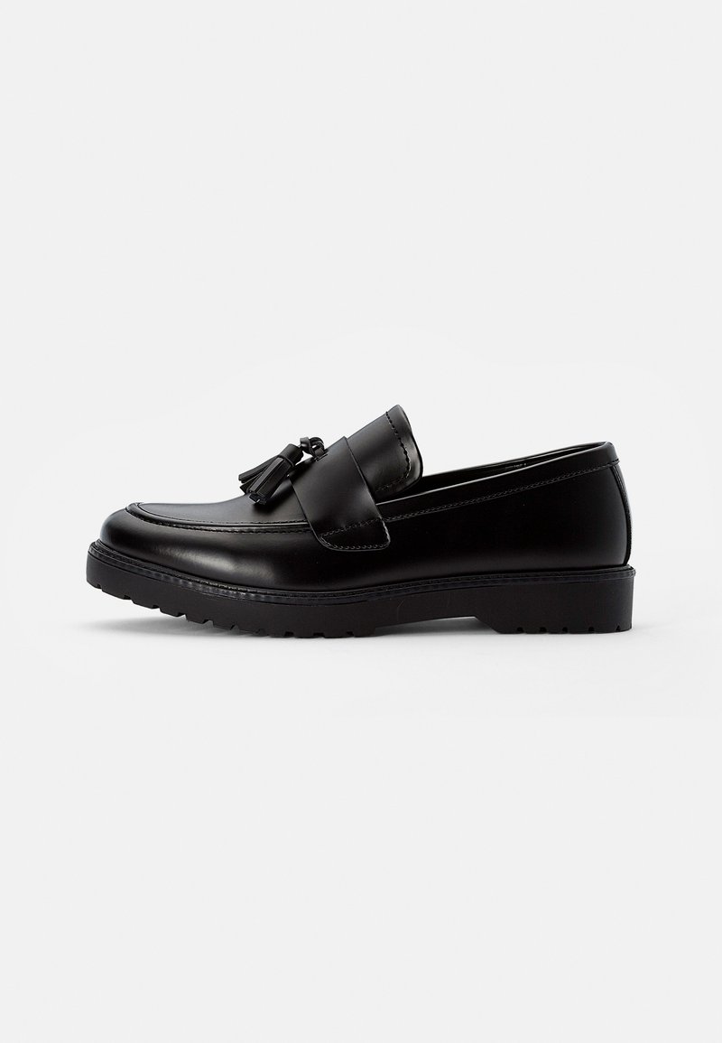 Black leather loafers with a flat sole, featuring a decorative tassel on the vamp and stitched detailing along the edges.