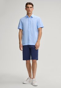 Lichtblauw kortarm overhemd met knopen, linnen uitstraling, gecombineerd met marineblauwe shorts en witte sneakers. Minimalistisch ontwerp, relaxed fit.