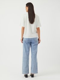 Hvitt bomull T-skjorte med korte ermer, kombinert med lyseblå vide jeans. Modellen har mørkebrunt hår og har på seg svarte blokkhelte sko.