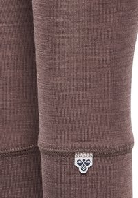 Bruna leggings gjorda av texturerat tyg, med dekorativ sömnad och en liten logotypetikett på nederkanten. Slät och figurnära design.