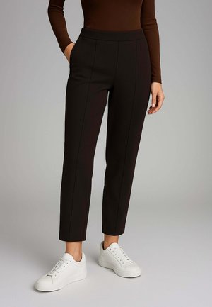 Pantaloni neri a sigaretta realizzati in un materiale morbido con una vita alta e tasche laterali, abbinati a sneakers bianche.