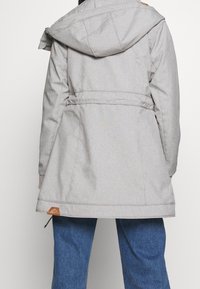 Light gray, hooded jacket with a fitted waist, two side pockets, and a brown label at the hem. Material appears smooth with a subtle texture.