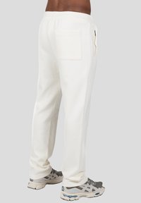 Witte sweatpants van zacht materiaal, met een achterzak, elastische tailleband en taps toelopende pijpen. Gemaakt in combinatie met grijze sportschoenen.