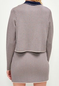 Koftklänning med långa ärmar som har ett rutigt mönster i röd, vit och marinblå färg. Kortad design med vågig marinblå krage och detaljer.