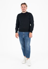 Pullover nero a maniche lunghe con texture a coste, abbinato a jeans in denim azzurro chiaro a gamba tapered e sneakers bianche. Design semplice e funzionale.