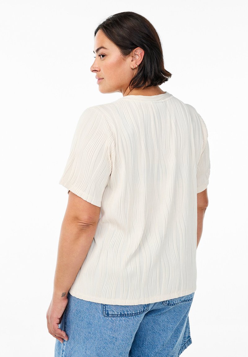 Kortärmad krämfärgad blus med en strukturerad, vågig mönstring och rund halsringning, kombinerad med blå denimshorts. Rent design, avslappnad passform.