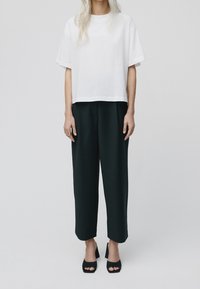 Camiseta blanca recortada de manga corta, combinada con pantalones de pierna ancha negros de talle alto y sandalias negras de tacón. Textura de tela suave.