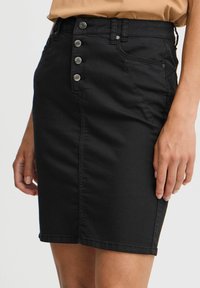 Black denim skirt featuring a fitted design, five-button front closure, and subtle side pockets. Smooth texture with minimal stitching details.