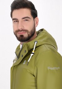 Zelena vodoodporna jakna s kapuco, opremljena z zadrgo, snap gumbi, belimi vrvicami in logotipom na prsih. Gladka tekstura in prilegajoča oblika.