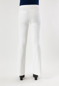 Pantaloni bianchi svasati in tessuto elasticizzato, con due tasche posteriori rifinite a contrasto, abbinati a scarpe nere con tacco alto.