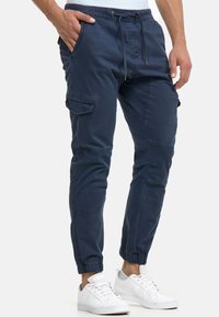 Granatowe spodnie cargo z mieszanki bawełny, z elastycznym pasem, sznurkiem do regulacji, zwężanymi nogawkami i bocznymi kieszeniami, w parze z białymi trampkami.