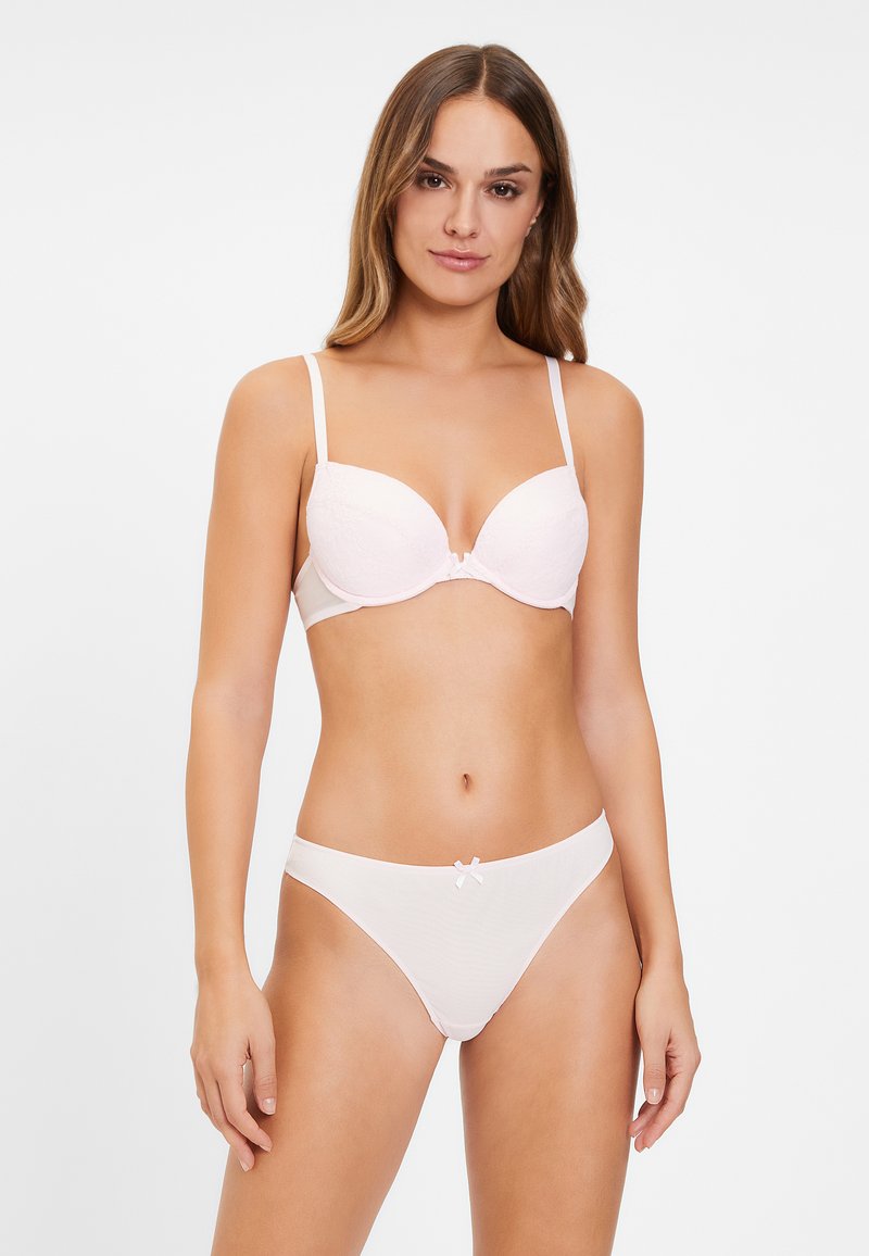 Lichtroze lingerie set bestaande uit een padded bh met kantstructuur en verstelbare banden, gecombineerd met bijpassende bikini slips met een klein strikdetail.