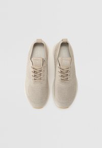 Beige Strick-Sneaker mit texturiertem Obermaterial, Schnürdesign und einer weichen Gummisohle. Verfügt über ein markantes Etikett mit dem Markenlogo.