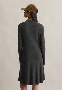 Abito in maglia grigia a coste con maniche lunghe, si allarga leggermente all'orlo. Abbinato a un cappello in corduroy marrone. Design semplice e strutturato.