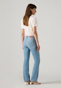 Jeans de tiro alto acampanados de color azul claro con bolsillos traseros y un parche de cuero en la cintura, combinados con una camiseta blanca sencilla.