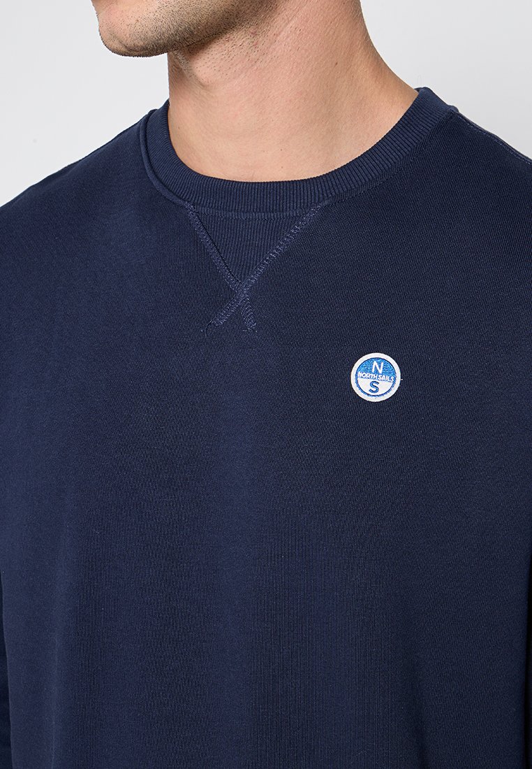 Felpa blu navy con collo rotondo, tessuto a trama e un piccolo logo circolare sul petto. Presenta un dettaglio cucito sul collo.