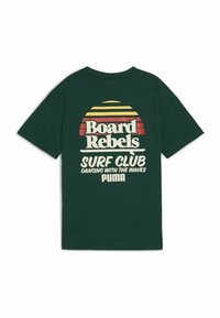 Camiseta de algodón verde oscuro con mangas cortas, que presenta un diseño gráfico en amarillo y rojo, mostrando "Board Rebels Surf Club" y "PUMA."