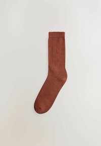 Brune ribbede sokker med en glat tekstur. Har en ensfarvet stil og et diskret logo på siden. Standard crew længde design.