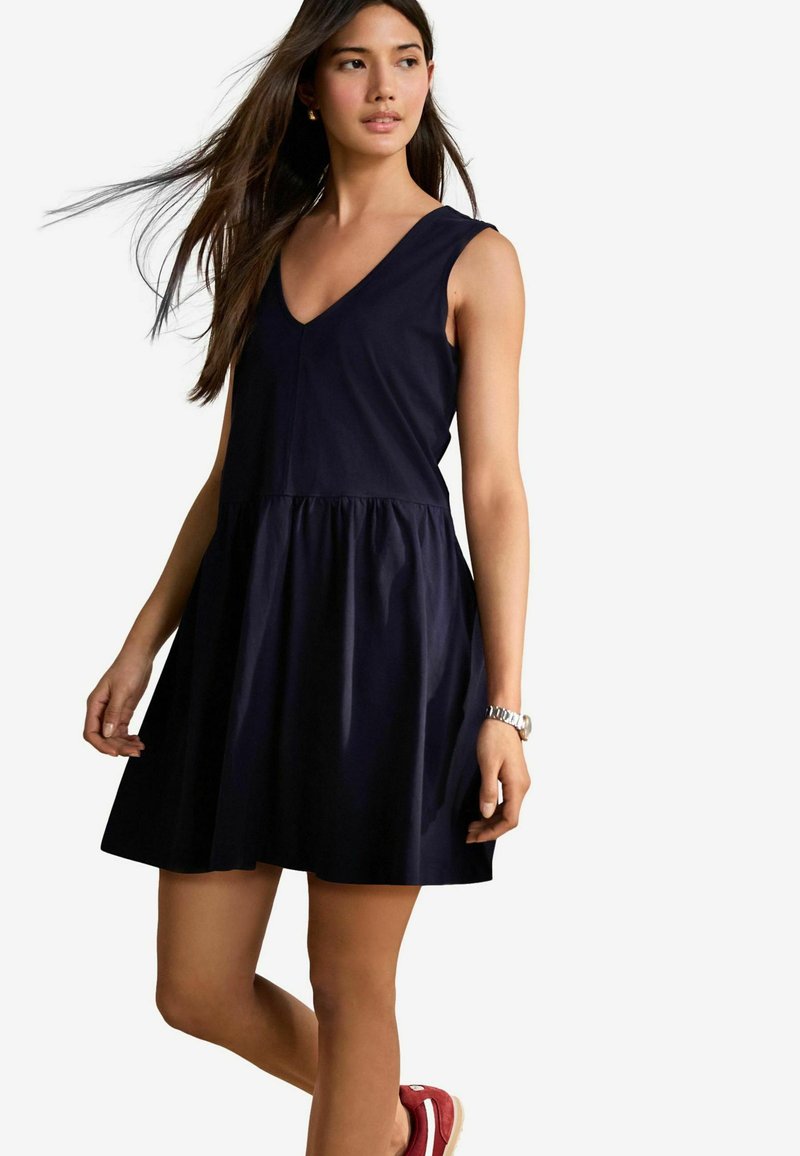 Robe sans manches bleu marine avec un décolleté en V et une taille froncée, en tissu doux. Associée à des chaussures rouge à enfiler.