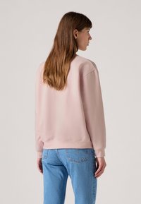 Sweatshirt rose avec un col rond, des poignets et un ourlet côtelés. Assorti à un jean texturé bleu clair, vu de l'arrière.