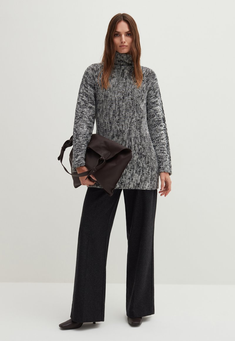 Gemütlicher Strickpullover in Grautönen mit hohem Kragen, kombiniert mit weit geschnittenen schwarzen Hosen und einer dunkelbraunen Lederhandtasche. Weiche Textur.