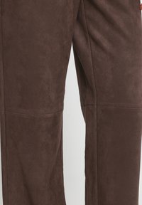 Gros plan d'un pantalon en daim marron montrant des coutures détaillées et une texture douce.