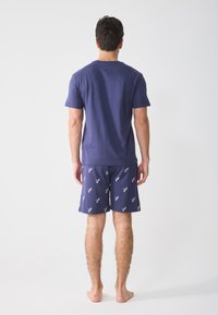 Marinblå bomulls t-shirt och mönstrade shorts. T-shirten har en klassisk rund hals; shortsen har ett fågelmotiv i vitt på en mörk bakgrund.