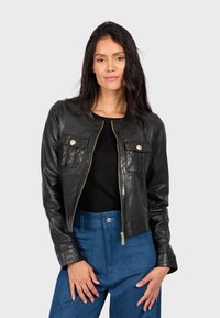 Černá kožená bunda se zipem, dvěma náprsními kapsami, kulatým límcem a strukturovaným střihem, v kombinaci s modrými džíny se zvýšeným pasem.